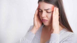 A young woman holding her temples with a pained expression, indicating she is suffering from a migraine headache