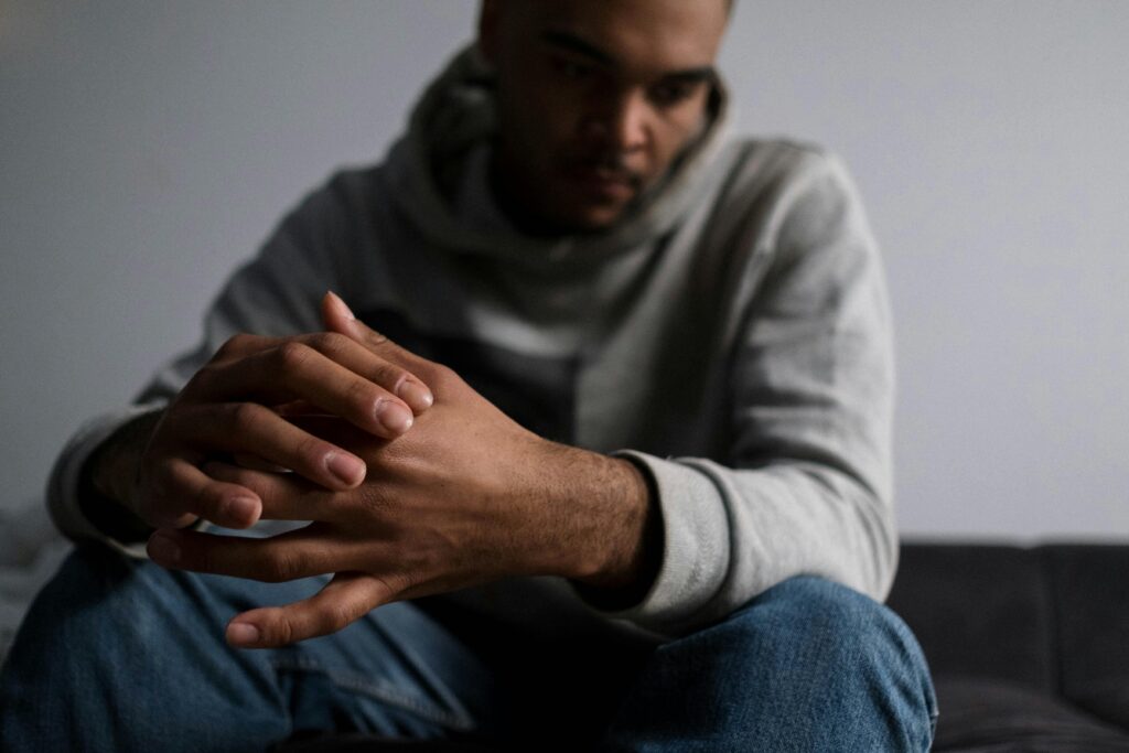 Man sitting with clasped hands, looking down in thought, reflecting anxiety and emotional struggle
