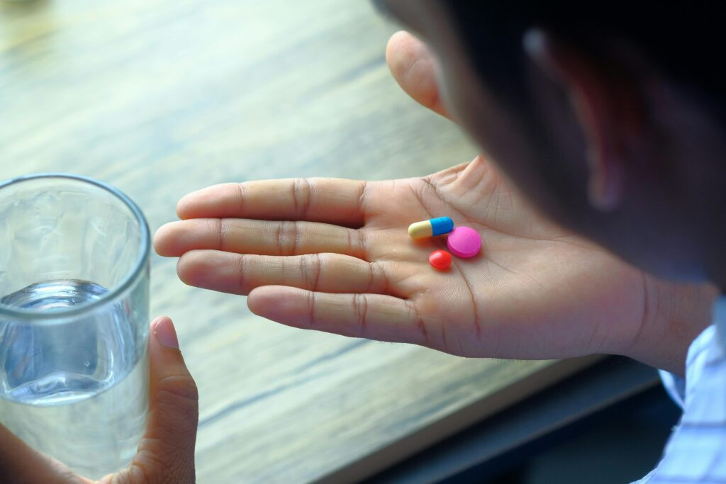 Close-up of a person holding colorful pills in one hand and a glass of water in the other, representing placebo effect and chronic pain treatments.