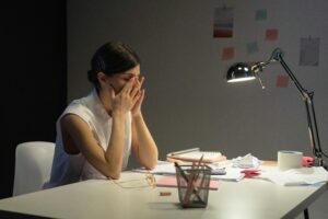 Woman sitting at a desk with her head in her hands, overwhelmed and anxious at night — representing the cycle of anxiety that won’t go away.