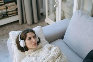 Woman lying on a couch wearing headphones, appearing withdrawn and feeling disconnected from emotions