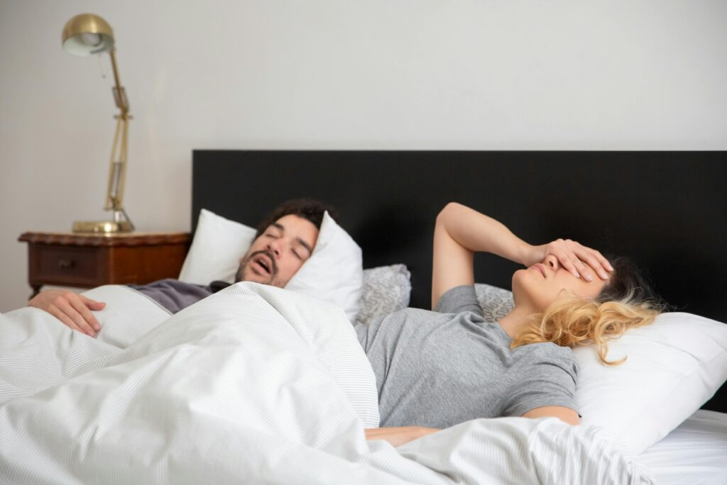 Woman frustrated in bed next to snoring partner, highlighting relationship and sleep challenges and sleep divorce