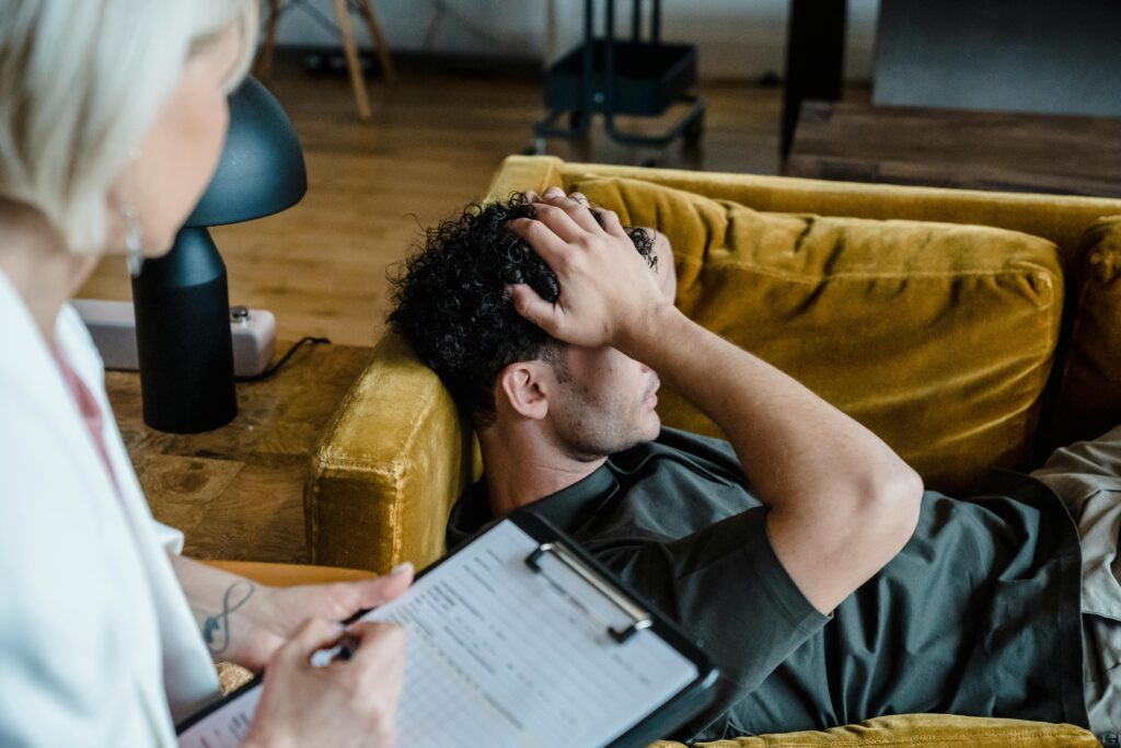 Therapist completing a sleep assessment form during a session as a client rests on a couch, illustrating why therapists ask about sleep patterns.