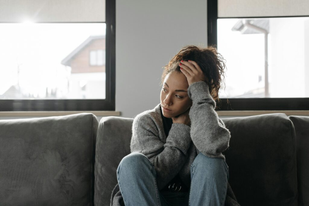 A woman sitting alone on a couch, reflecting quietly while living with chronic pain and social isolation.
