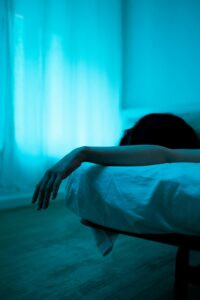 Person lying awake in bed at night with arm hanging off the mattress, illustrating insomnia and the question of when to see a therapist for sleep problems.