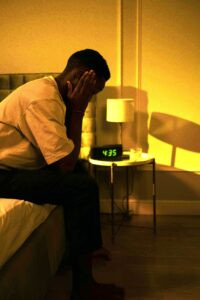 Woman sitting on edge of bed at 4:35am unable to fall back asleep during early morning awakening