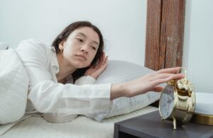 why do i wake up with anxiety featured. woman waking up and looking at her alarm clock with anxiety.